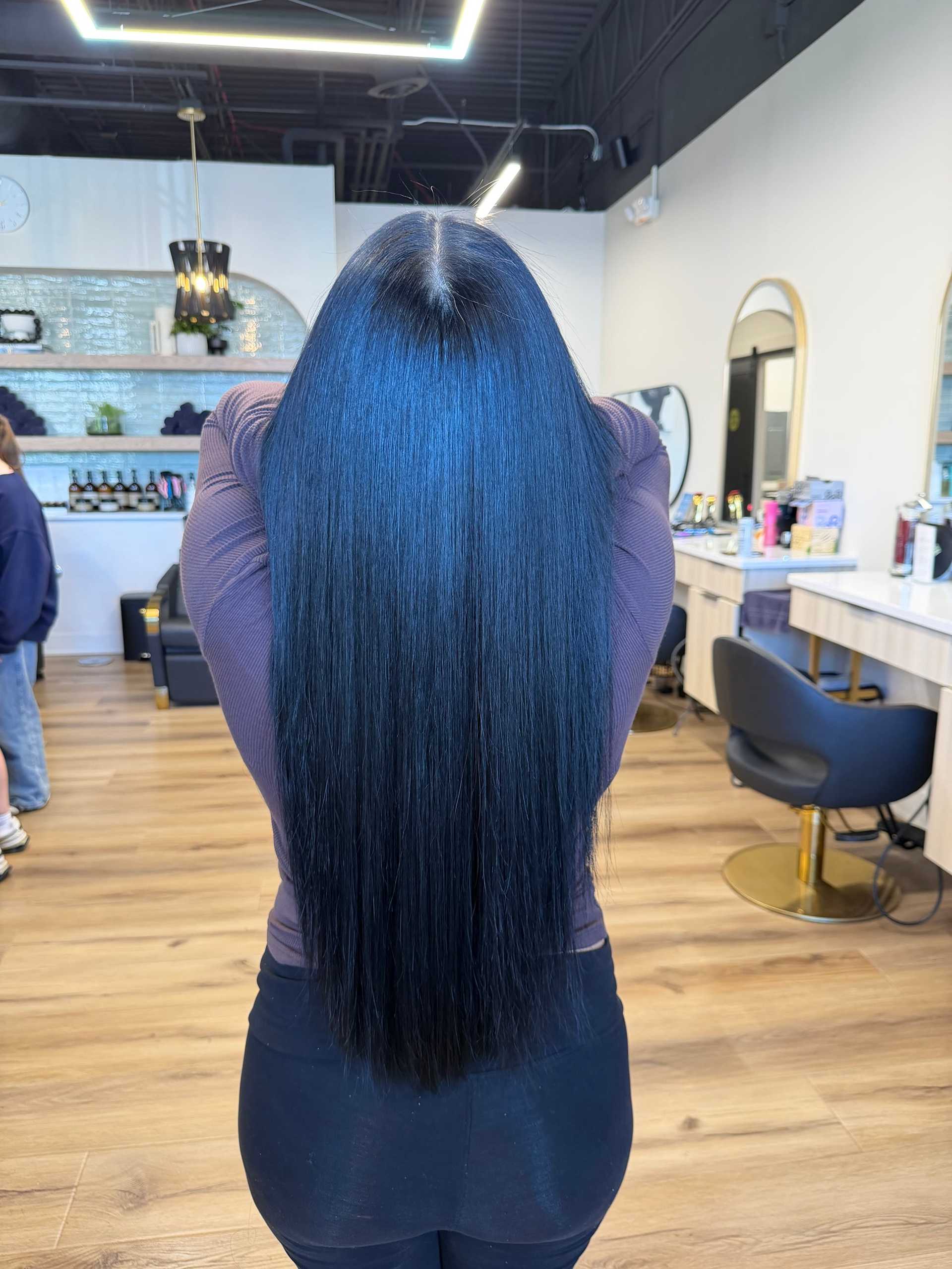 Long, straight black hair styled in a modern salon with wooden floors and elegant decor.