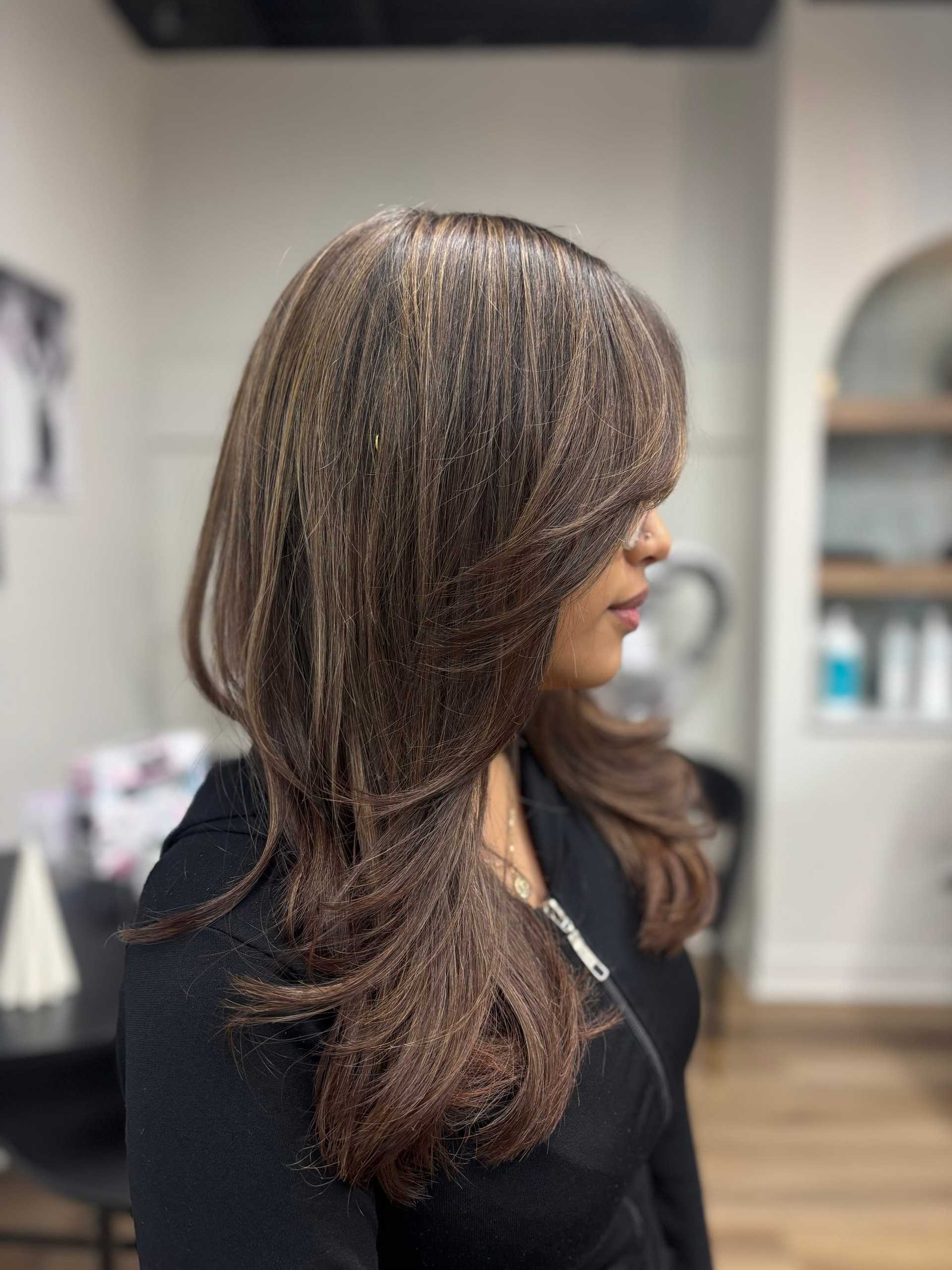 Woman with layered brown hair and highlights in a salon setting.