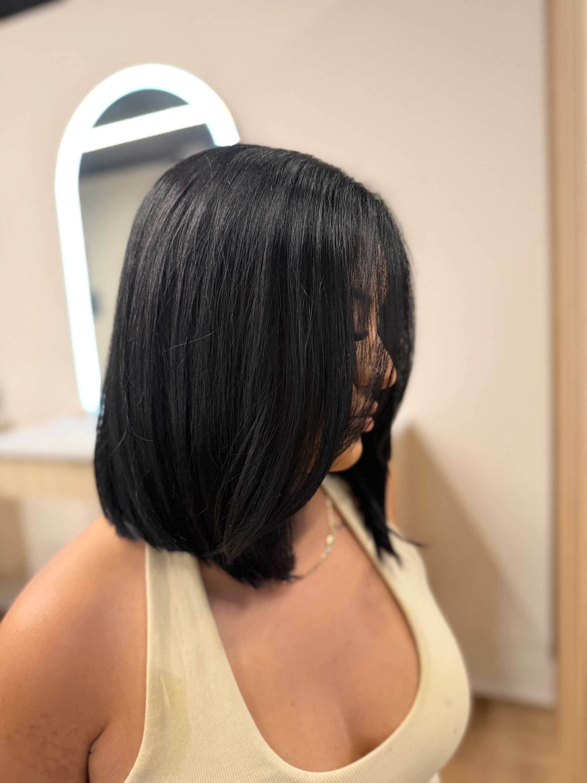 Woman with sleek bob haircut wearing a beige tank top, in a salon. Modern mirror in background.