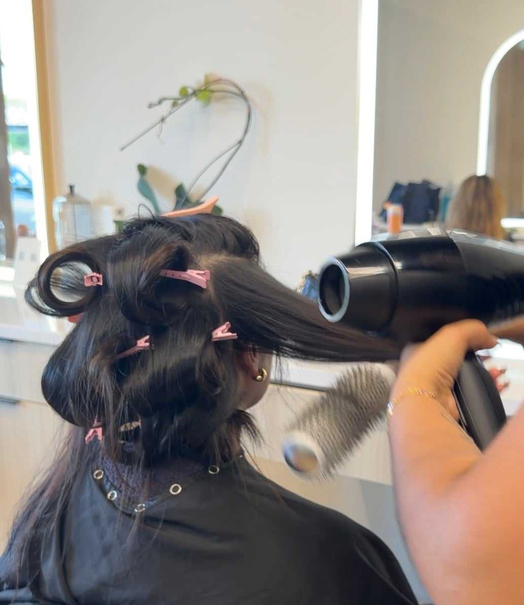 Hair salon styling session with roller clips, hairdryer, and round brush being used.