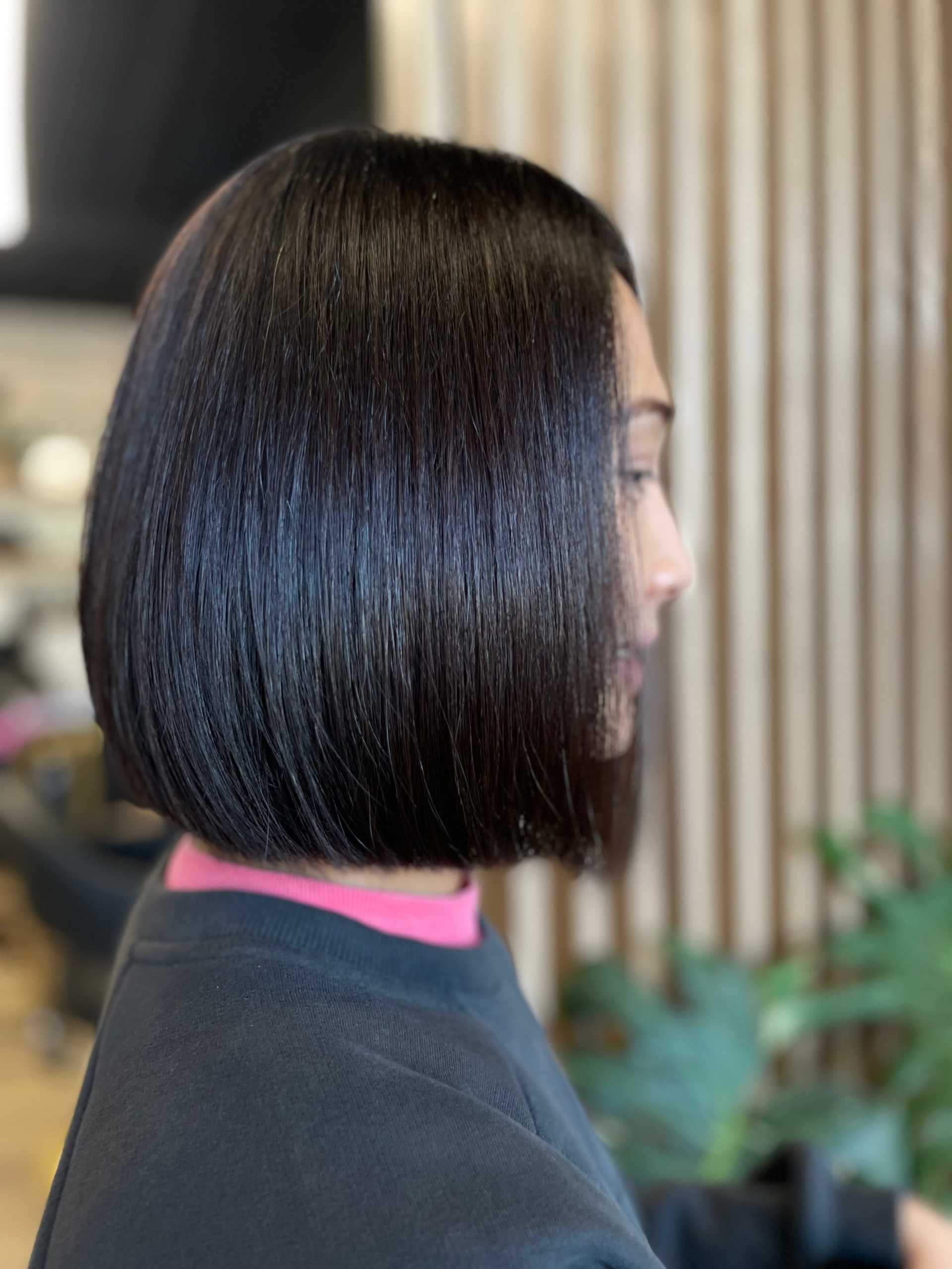 Sleek bob haircut on a woman with shiny, dark hair in a salon setting.