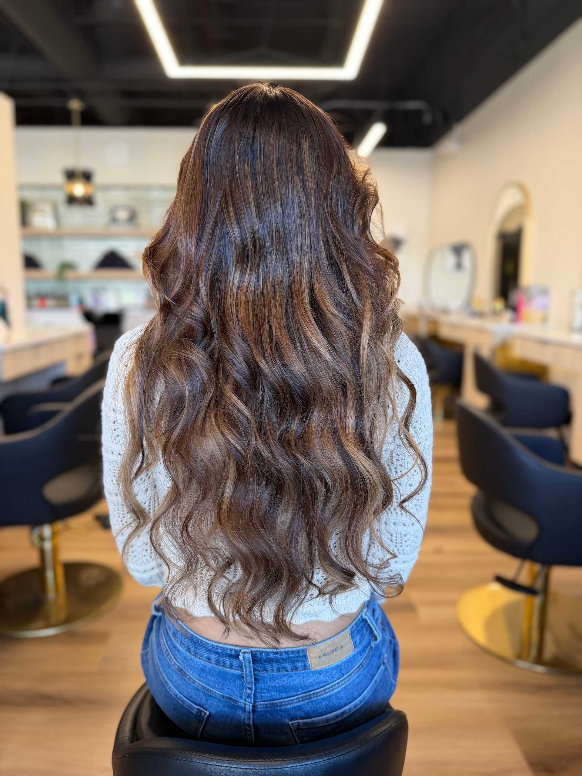 Long wavy hair cascading down the back of a person seated in a stylish salon.