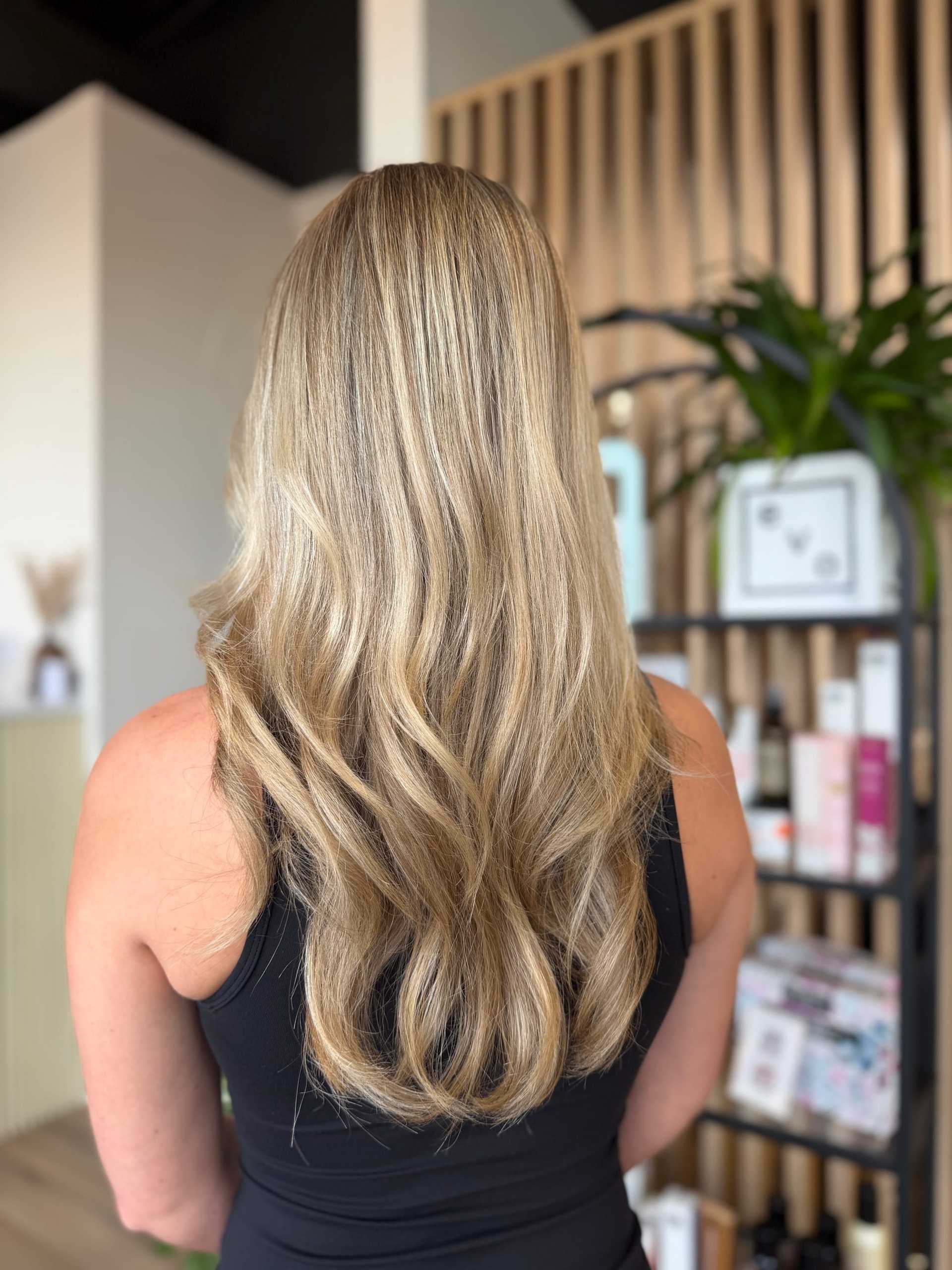 Wavy blonde hair from the back at a salon with products on display.